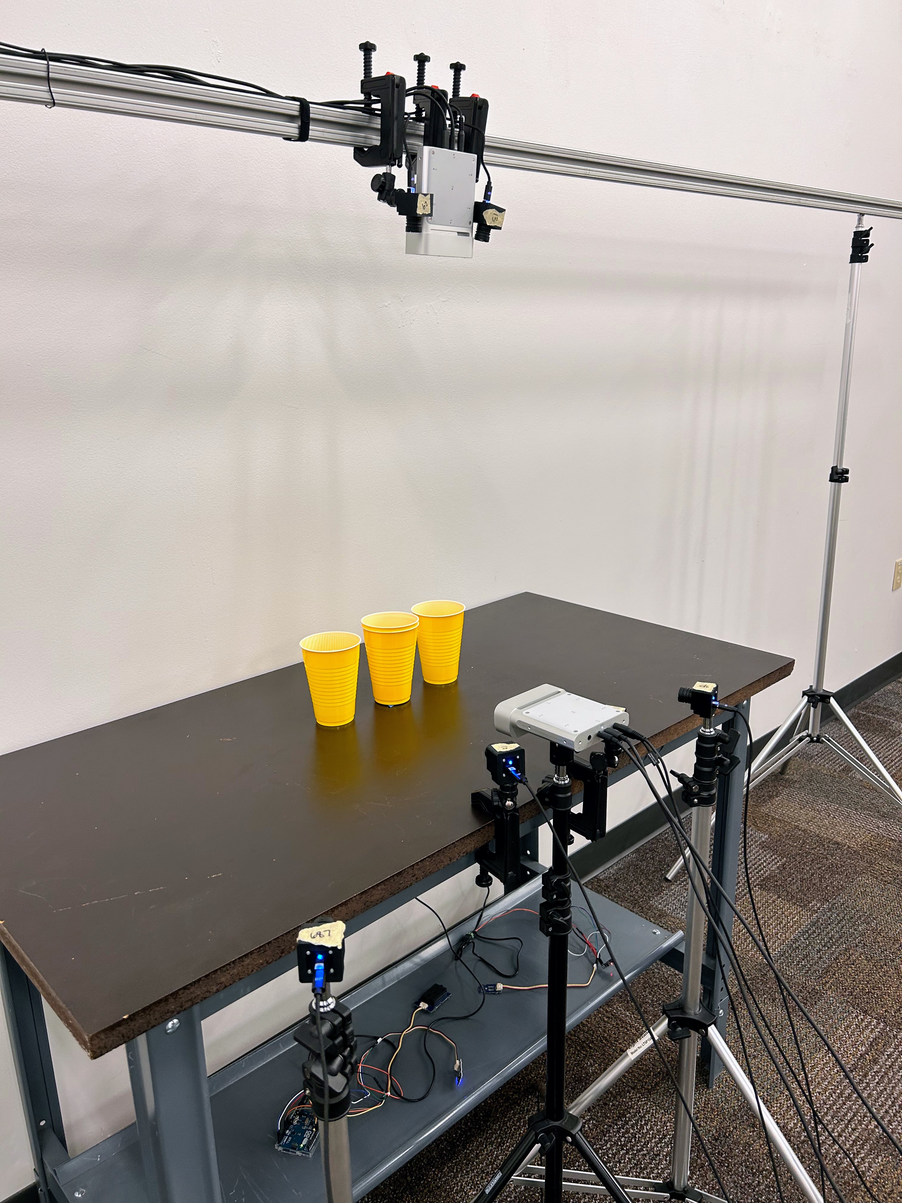 cameras in different directions are pointing at 3 plastic yellow cups on a table